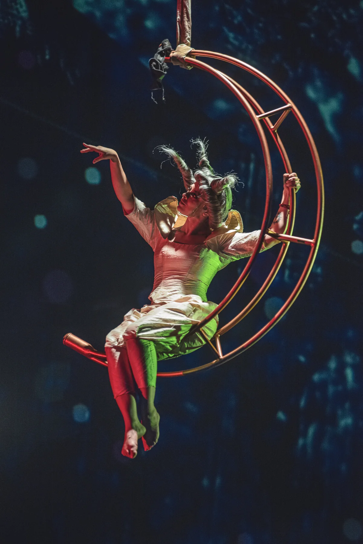 Un intérprete vestido de rojo realiza una figura en una estructura circular suspendida.